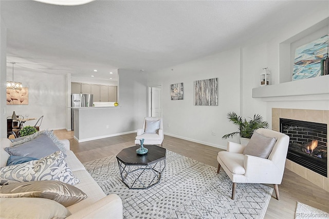 living room featuring a tiled fireplace, light hardwood / wood-style flooring, a textured ceiling, and a notable chandelier