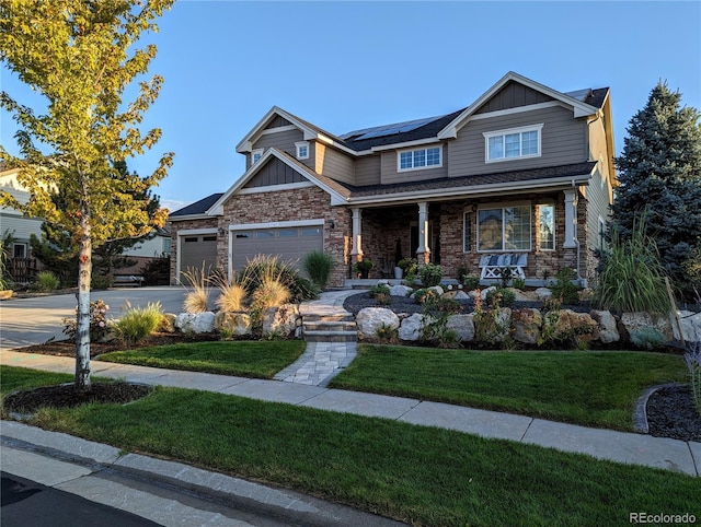 craftsman inspired home with a porch, stone siding, driveway, roof mounted solar panels, and a front lawn