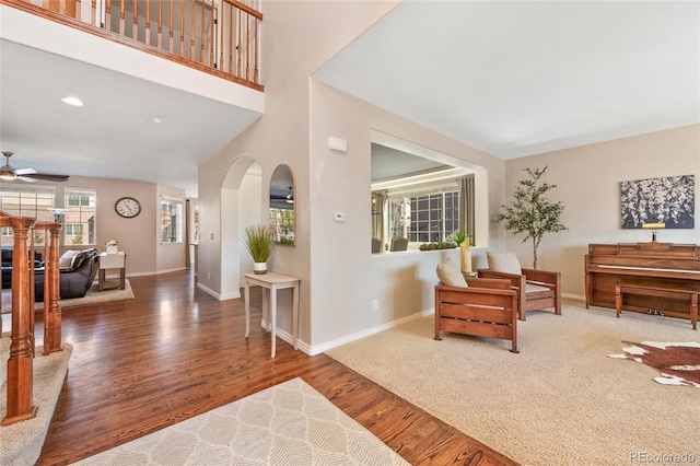 sitting room featuring arched walkways, a high ceiling, ceiling fan, wood finished floors, and baseboards