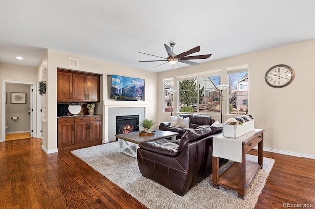 living area with dark wood-style flooring, a fireplace, visible vents, and baseboards