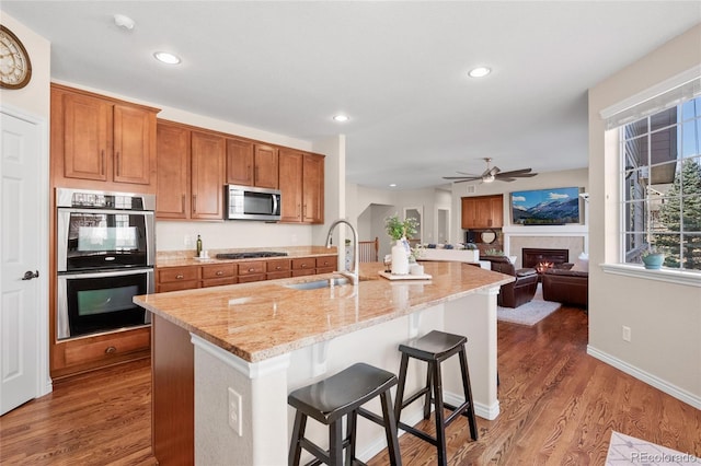 kitchen featuring stainless steel appliances, wood finished floors, a sink, brown cabinets, and a glass covered fireplace