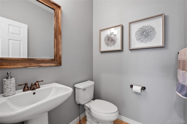 half bath with baseboards, a sink, and toilet