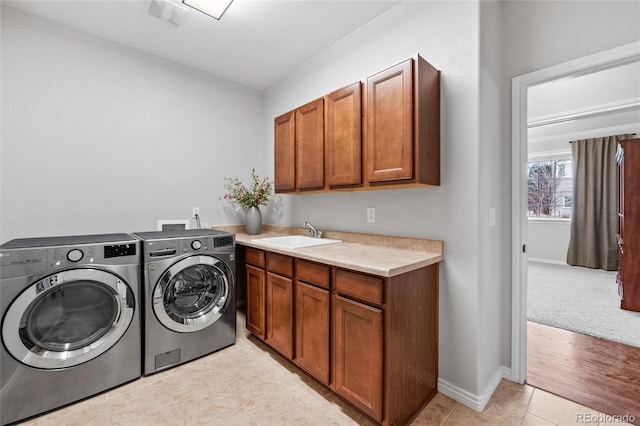 clothes washing area with cabinet space, light tile patterned floors, baseboards, washing machine and dryer, and a sink