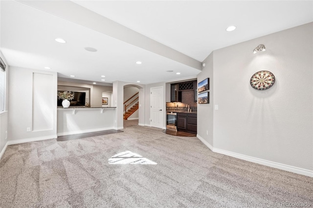 unfurnished living room with baseboards, stairway, wet bar, carpet floors, and recessed lighting