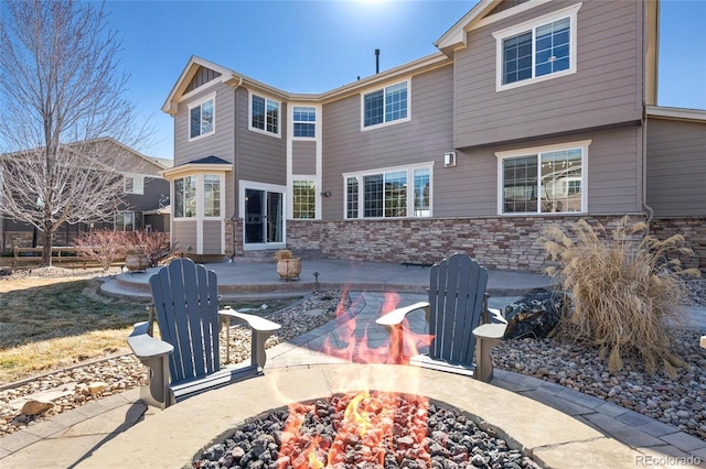 rear view of property with a patio area, an outdoor fire pit, and stone siding