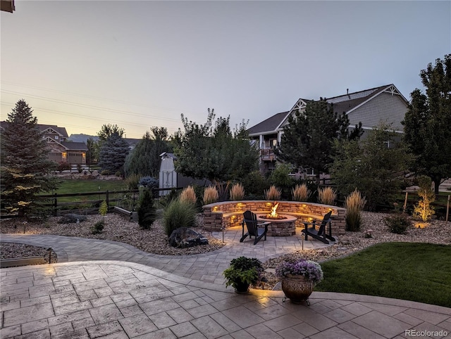 patio terrace at dusk featuring an outdoor fire pit, a lawn, and fence