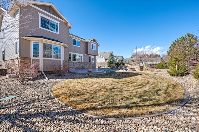 back of property featuring stone siding, a lawn, a residential view, board and batten siding, and a patio area