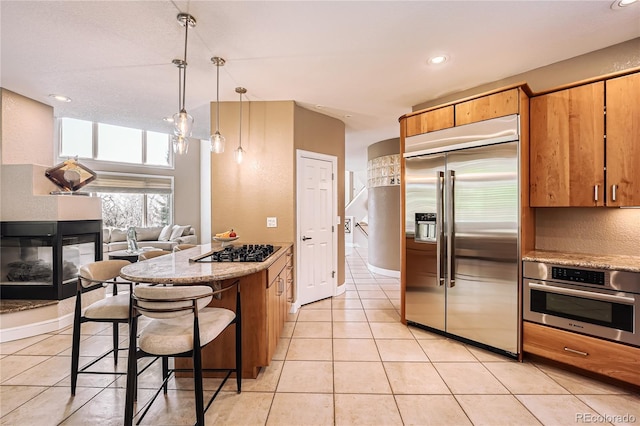 6961 Salvia St, Arvada, CO 80007 - kitchen featuring stainless steel appliances, light tile patterned floors, a tile fireplace, a kitchen bar, and recessed lighting