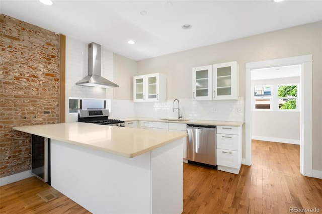 1753 W 36th Ave, Denver, CO 80211 - kitchen featuring stainless steel appliances, wall chimney range hood, a peninsula, glass insert cabinets, and white cabinetry