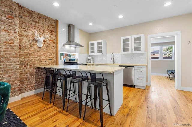 1753 W 36th Ave, Denver, CO 80211 - kitchen featuring wall chimney range hood, appliances with stainless steel finishes, a kitchen bar, white cabinetry, and recessed lighting