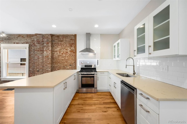1753 W 36th Ave, Denver, CO 80211 - kitchen with wall chimney exhaust hood, appliances with stainless steel finishes, a peninsula, light countertops, and light wood-type flooring
