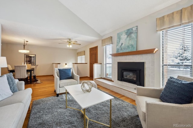 living area featuring ceiling fan, a tiled fireplace, vaulted ceiling, and wood finished floors