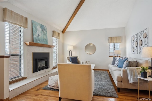 living area with vaulted ceiling with beams, light wood finished floors, a tile fireplace, and baseboards