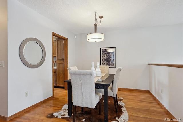 dining space with a textured ceiling, baseboards, and light wood-style floors