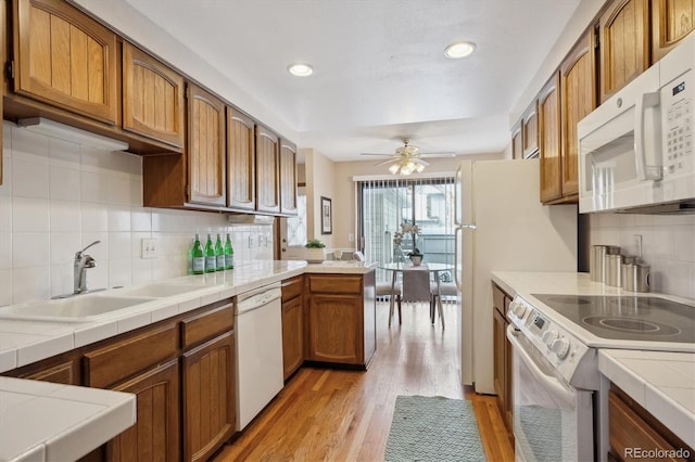 kitchen with white appliances, brown cabinetry, a sink, and tile counters