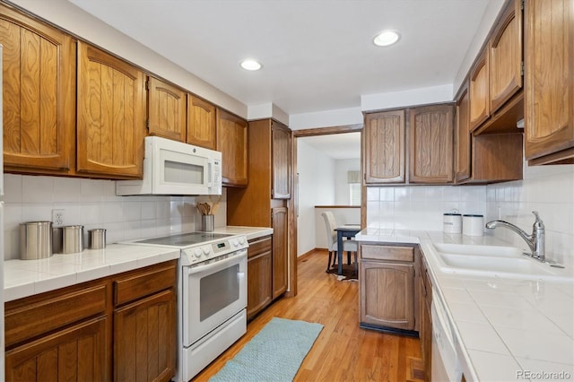 kitchen featuring tile countertops, brown cabinetry, light wood-style floors, a sink, and white appliances