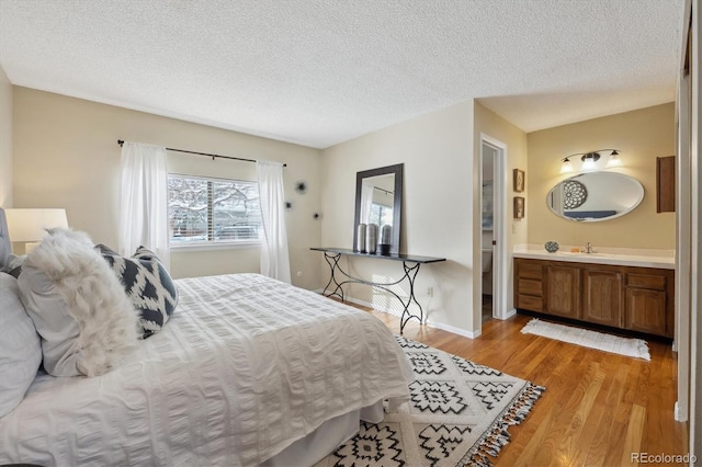 bedroom with ensuite bath, light wood-style flooring, baseboards, and a textured ceiling