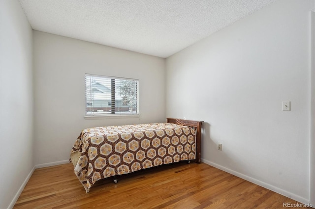 bedroom with a textured ceiling, light wood-type flooring, and baseboards