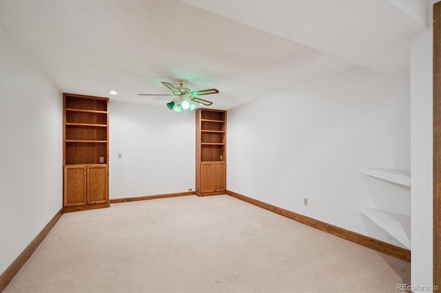 spare room with built in shelves, light carpet, baseboards, and a ceiling fan