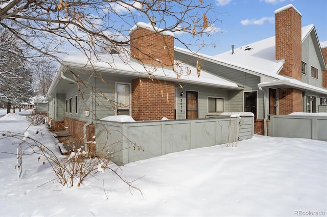 snow covered back of property featuring a chimney and brick siding