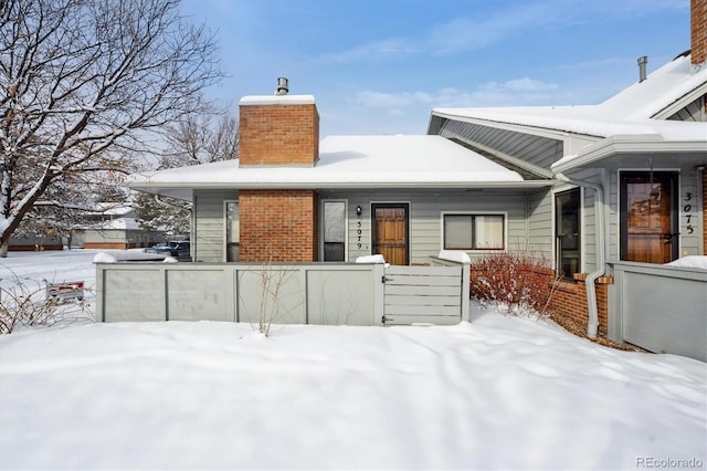 snow covered property with a fenced front yard, a chimney, and brick siding