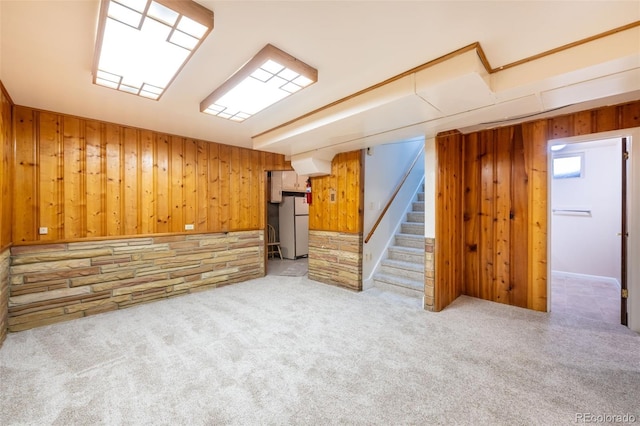 basement featuring light carpet, white refrigerator, and wood walls