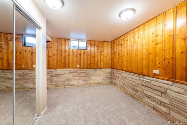 basement with a healthy amount of sunlight, light carpet, and wooden walls