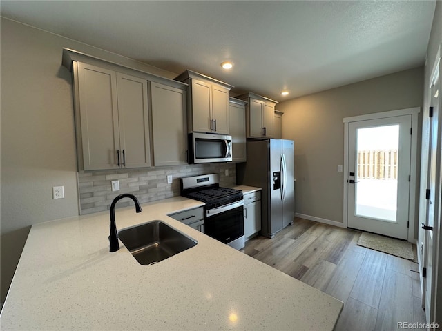 kitchen featuring tasteful backsplash, gray cabinets, appliances with stainless steel finishes, light wood-style floors, and a sink