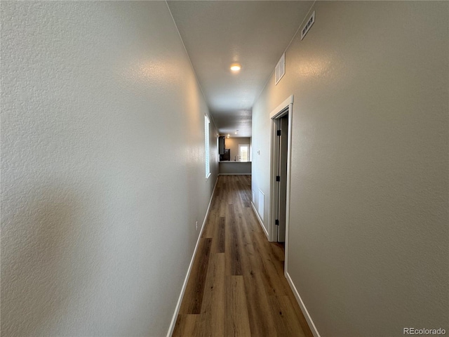 hall with visible vents, baseboards, and wood finished floors