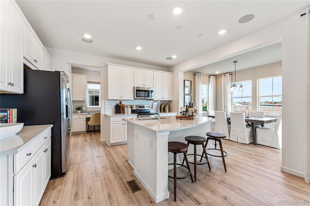 kitchen featuring a center island with sink, appliances with stainless steel finishes, hanging light fixtures, light countertops, and a sink