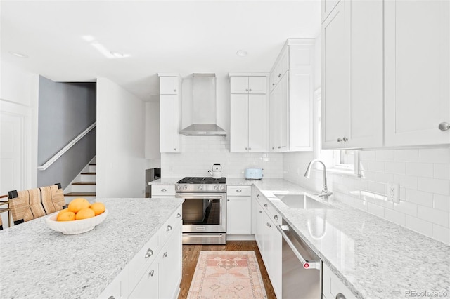 kitchen with light stone countertops, sink, white cabinets, appliances with stainless steel finishes, and wall chimney range hood