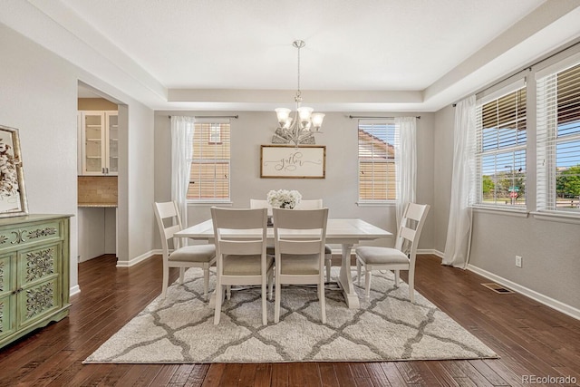 dining space featuring an inviting chandelier, dark hardwood / wood-style floors, and a raised ceiling