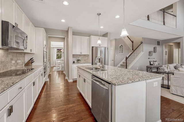 kitchen with appliances with stainless steel finishes, dark hardwood / wood-style floors, pendant lighting, white cabinetry, and an island with sink