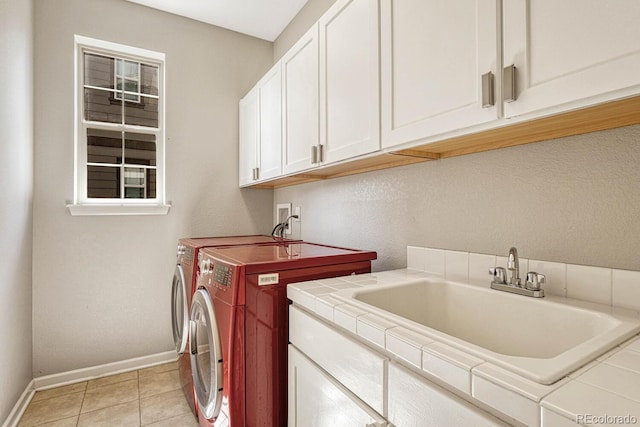 clothes washing area featuring light tile patterned floors, sink, washer and clothes dryer, and cabinets