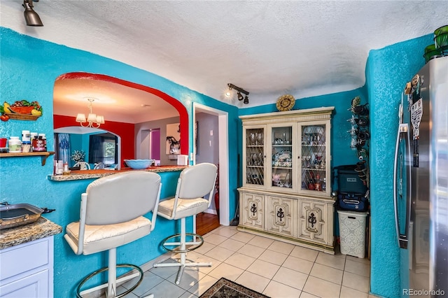 655 S Perry St, Denver, CO 80219 - interior space featuring track lighting, arched walkways, freestanding refrigerator, a textured ceiling, and light tile patterned flooring