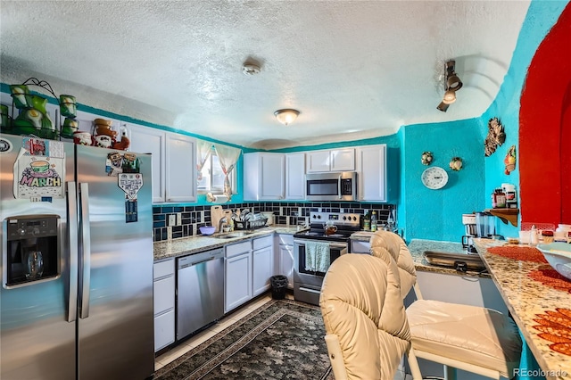 655 S Perry St, Denver, CO 80219 - kitchen featuring a textured ceiling, backsplash, white cabinets, and stainless steel appliances
