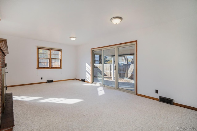 spare room featuring a brick fireplace and light carpet