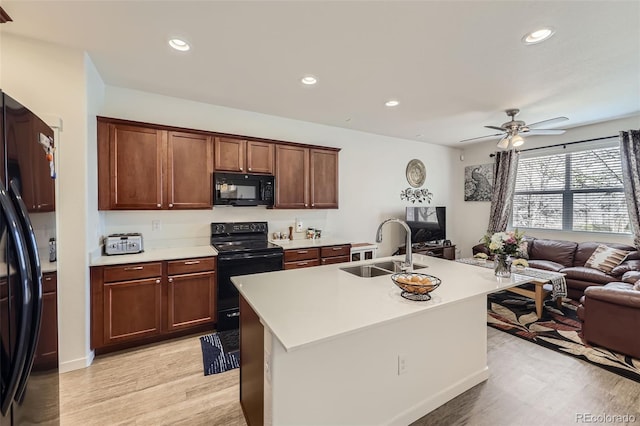 kitchen featuring light wood finished floors, a sink, open floor plan, light countertops, and black appliances