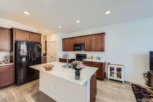 kitchen with black appliances, a center island with sink, light wood finished floors, and light countertops