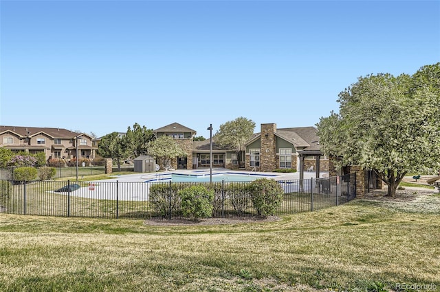 community pool with a lawn, fence, a residential view, and a storage shed