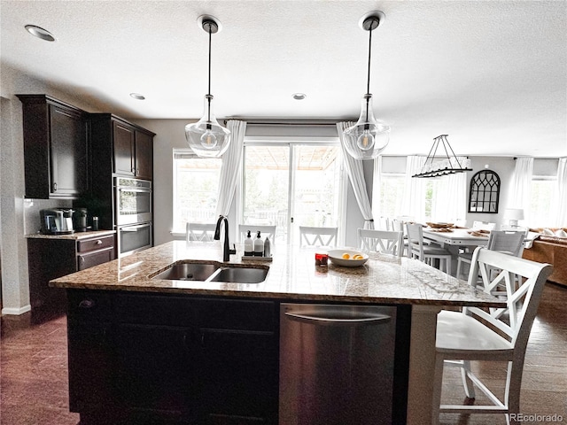 15468 W 50th Pl, Golden, CO 80403 - kitchen with stainless steel appliances, a center island with sink, light stone countertops, open floor plan, and hanging light fixtures