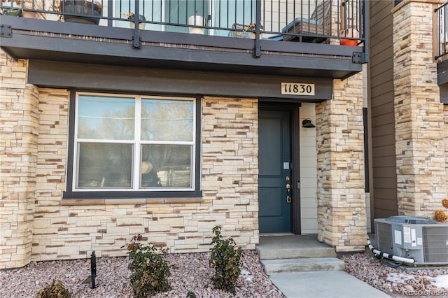 property entrance featuring a balcony, stone siding, and central AC unit