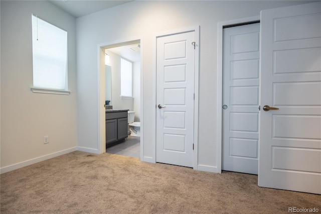 unfurnished bedroom featuring baseboards, light carpet, and ensuite bath