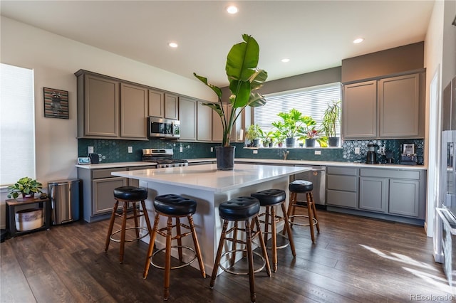 kitchen featuring a breakfast bar area, a center island, stainless steel appliances, light countertops, and gray cabinetry