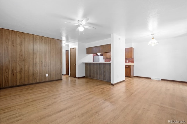 unfurnished living room with light hardwood / wood-style floors, ceiling fan, and wood walls