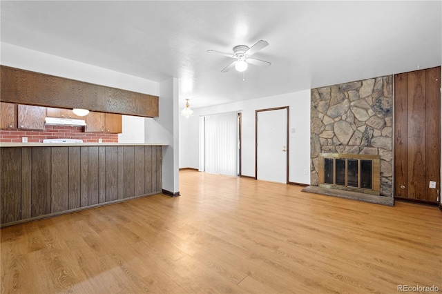 unfurnished living room with ceiling fan, a stone fireplace, and light wood-type flooring