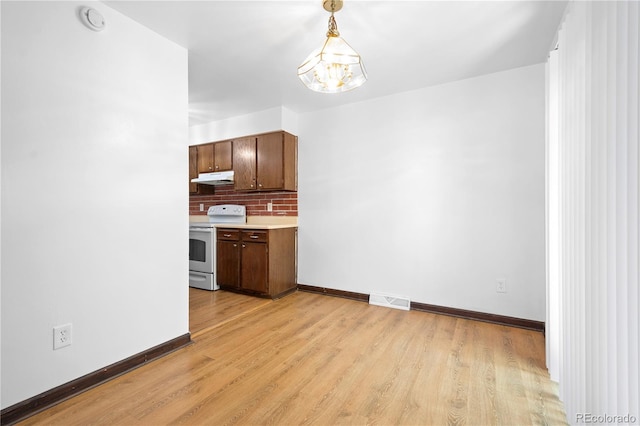 kitchen featuring light wood-type flooring, tasteful backsplash, decorative light fixtures, an inviting chandelier, and white electric range