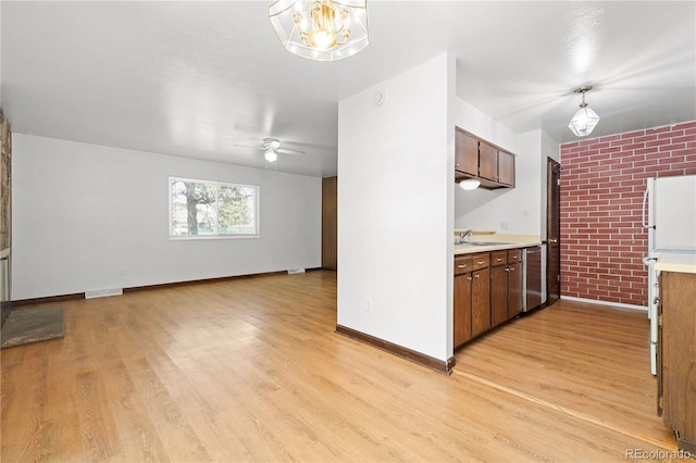 kitchen featuring dishwasher, sink, brick wall, pendant lighting, and light hardwood / wood-style floors