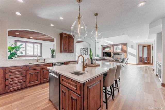 kitchen featuring dishwasher, sink, light wood-type flooring, an island with sink, and tasteful backsplash