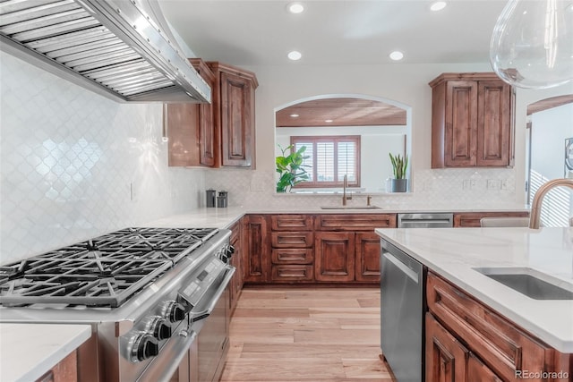 kitchen featuring backsplash, exhaust hood, sink, light wood-type flooring, and appliances with stainless steel finishes